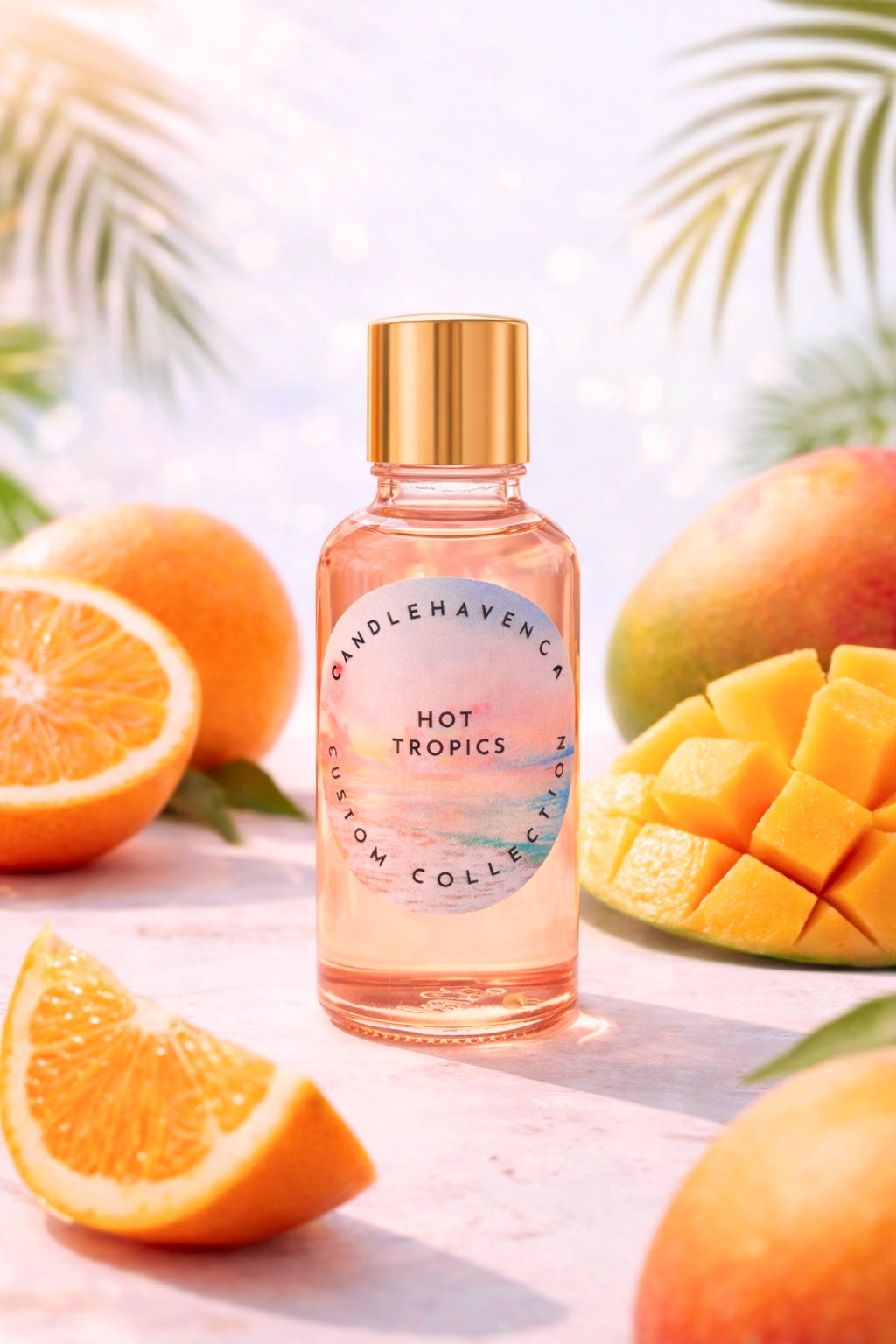 Pink candle fragrance oil bottle labeled 'Hot Tropics' surrounded by oranges and mangoes on a light background