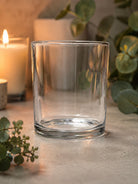 Clear glass candle vessel on a surface with candles and eucalyptus leaves in the background