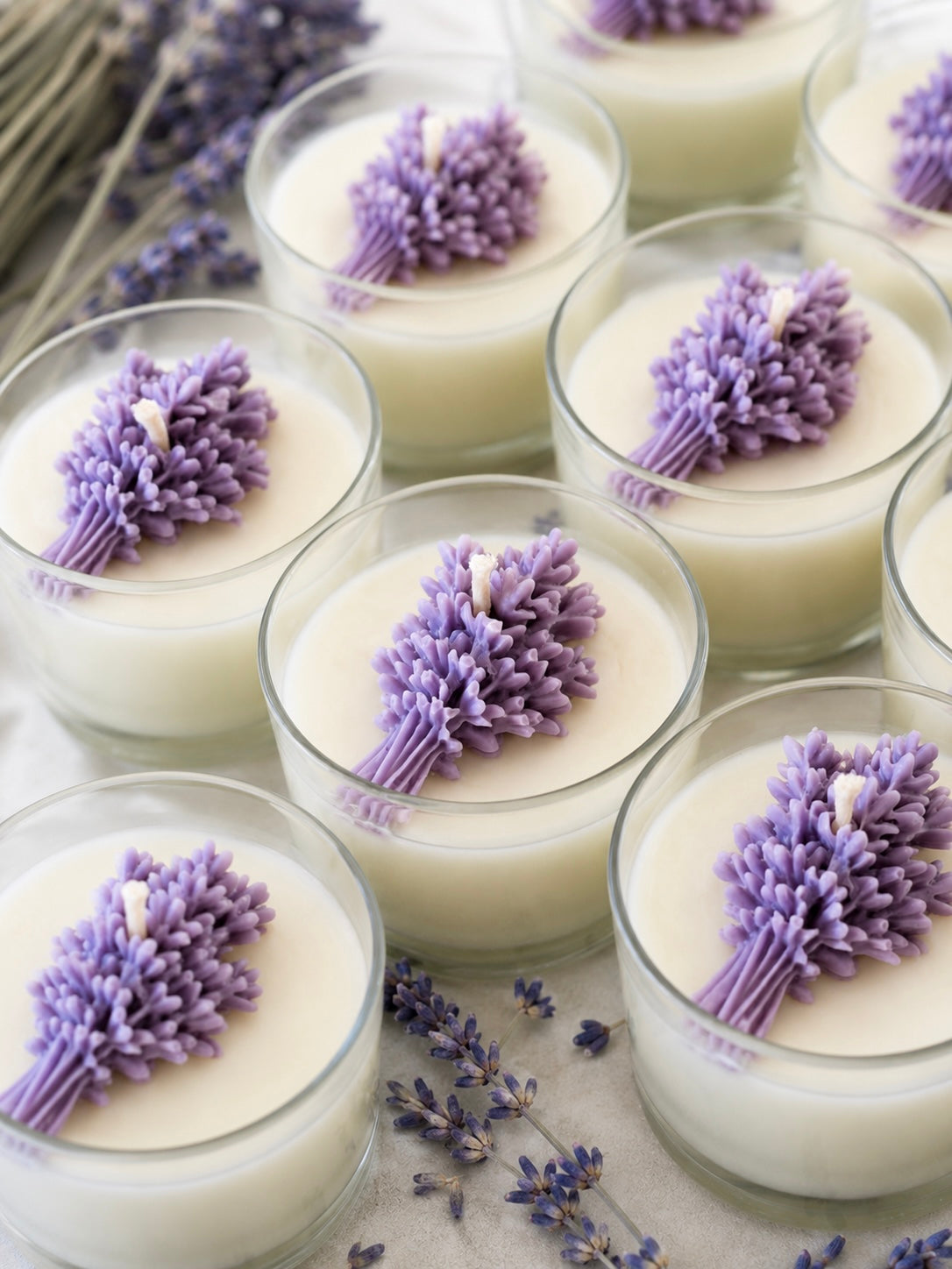 Candles with lavender flowers in glass containers on a wooden surface with lavender buds.