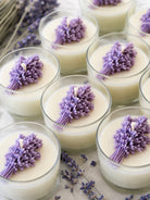 Candles with lavender flowers in glass containers on a wooden surface with lavender buds.
