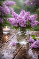 Lilac Rain for scented candle making | Bouquet of purple flowers in a clear vase on a wooden table with a candle in the background.