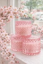 Set of three pink candle vessels on a windowsill with cherry blossoms.