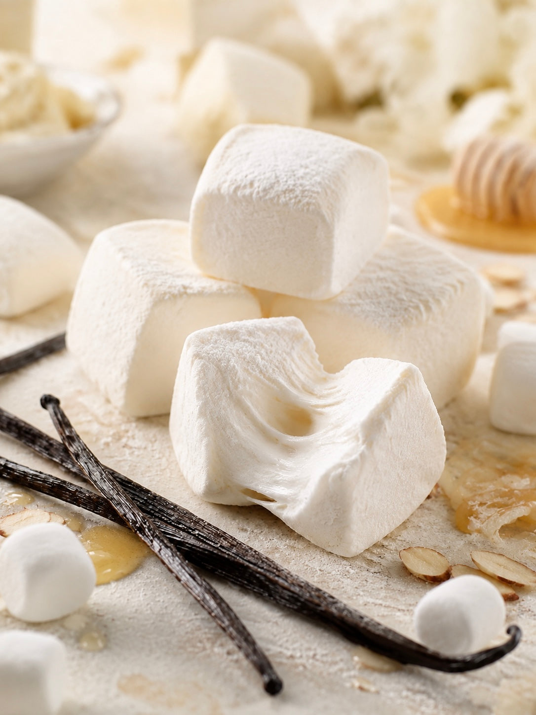 Soft white marshmallows on a lightly dusted surface with vanilla beans, honey, and a few small marshmallows nearby in a warm, styled food scene depicting Marshmallow Vanilla thrilla fragrance oil for candle making.