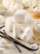 Soft white marshmallows on a lightly dusted surface with vanilla beans, honey, and a few small marshmallows nearby in a warm, styled food scene depicting Marshmallow Vanilla thrilla fragrance oil for candle making.