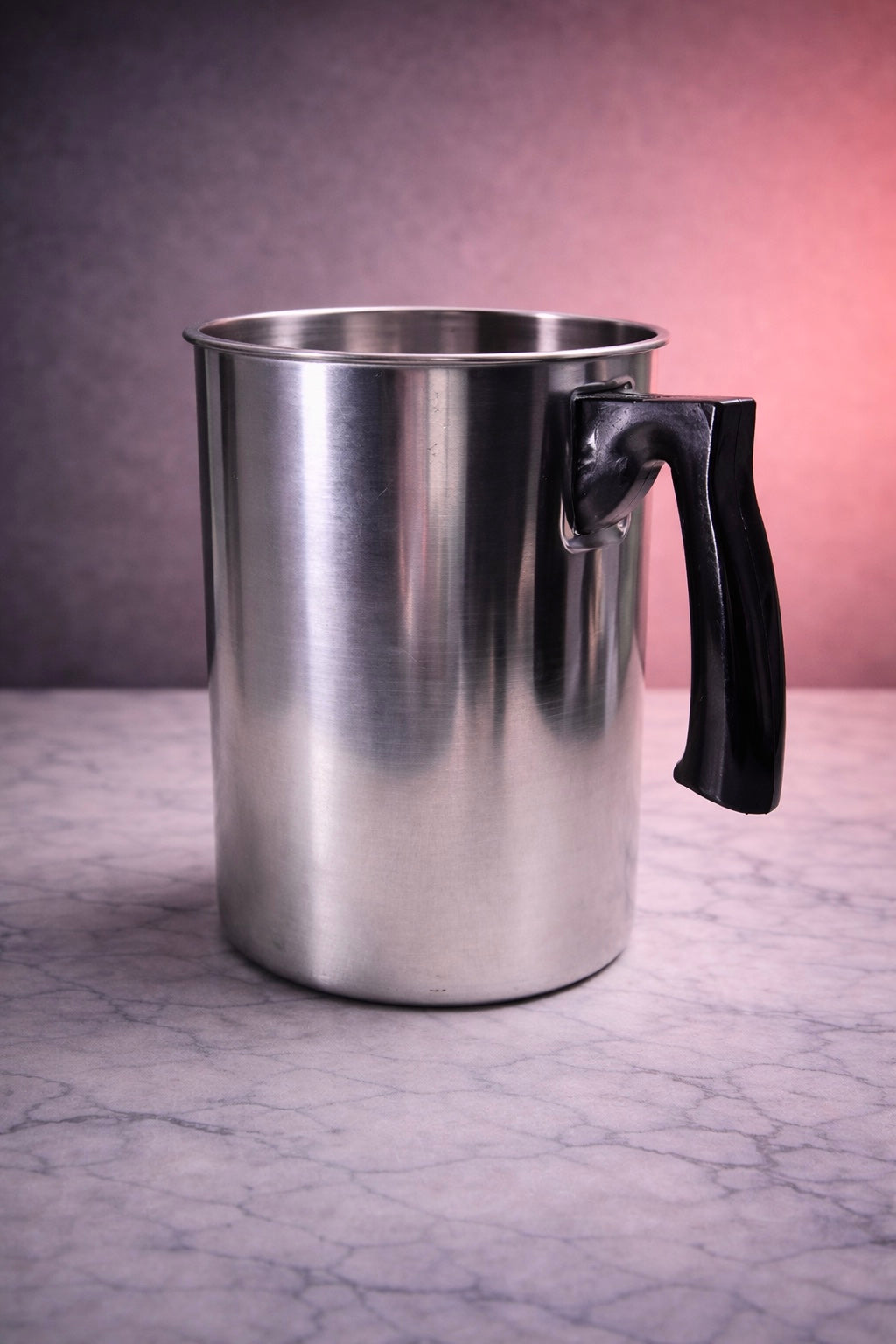 Metal pour pitcher with a black handle on a marble surface used for candle pouring
