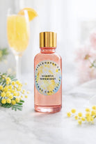 Bottle of 'Mimosa Mornings' fragrance oil with a gold cap on a light background