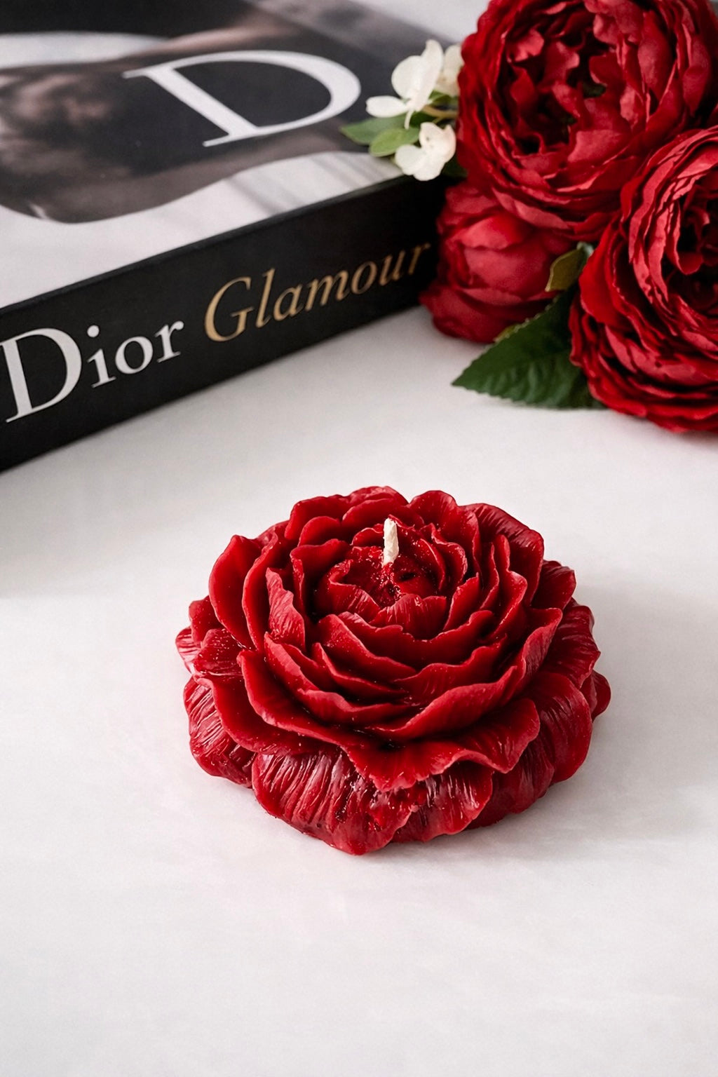 Peony shaped candle on a white surface with a Dior Glamour magazine in the background.