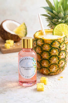 Pina Colada-themed candle fragrance oil in a pink bottle on a white surface with pineapple and coconut elements.