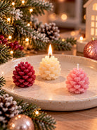 Three pinecone candles
One creamy white, one plum coloured and one pink on a plate. Christmas decor is in the background 