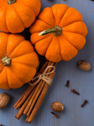 Three small pumpkins with cinnamon sticks and nuts on a blue surface depicting a pumpkin clove fragrance oil