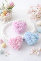 Heart-shaped wax roses in pink and blue on a white surface with flowers and eggs.