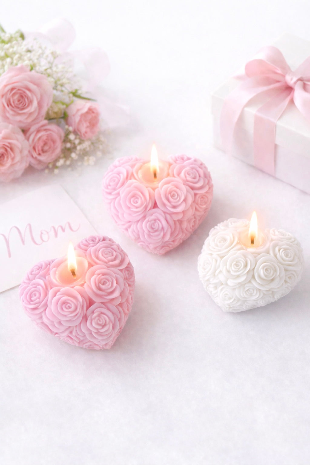 Heart-shaped rose candles on a white surface with pink roses and a gift box in the background.