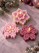 Three lit snowflake candles in blush pink, lavender and plum, made with decorative snowflake candle molds and displayed on a softly styled Christmas tabletop.