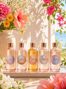 Five candle fragrance oil bottles with circular labels on a wooden surface, surrounded by flowers.