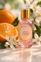 Pink bottle labeled 'Sunlit Orange Blossom' with oranges and flowers in the background
