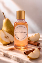 Bottle of 'Sweet Cinnamon Pear' candle fragrance oil with pears and cinnamon sticks on a wooden surface