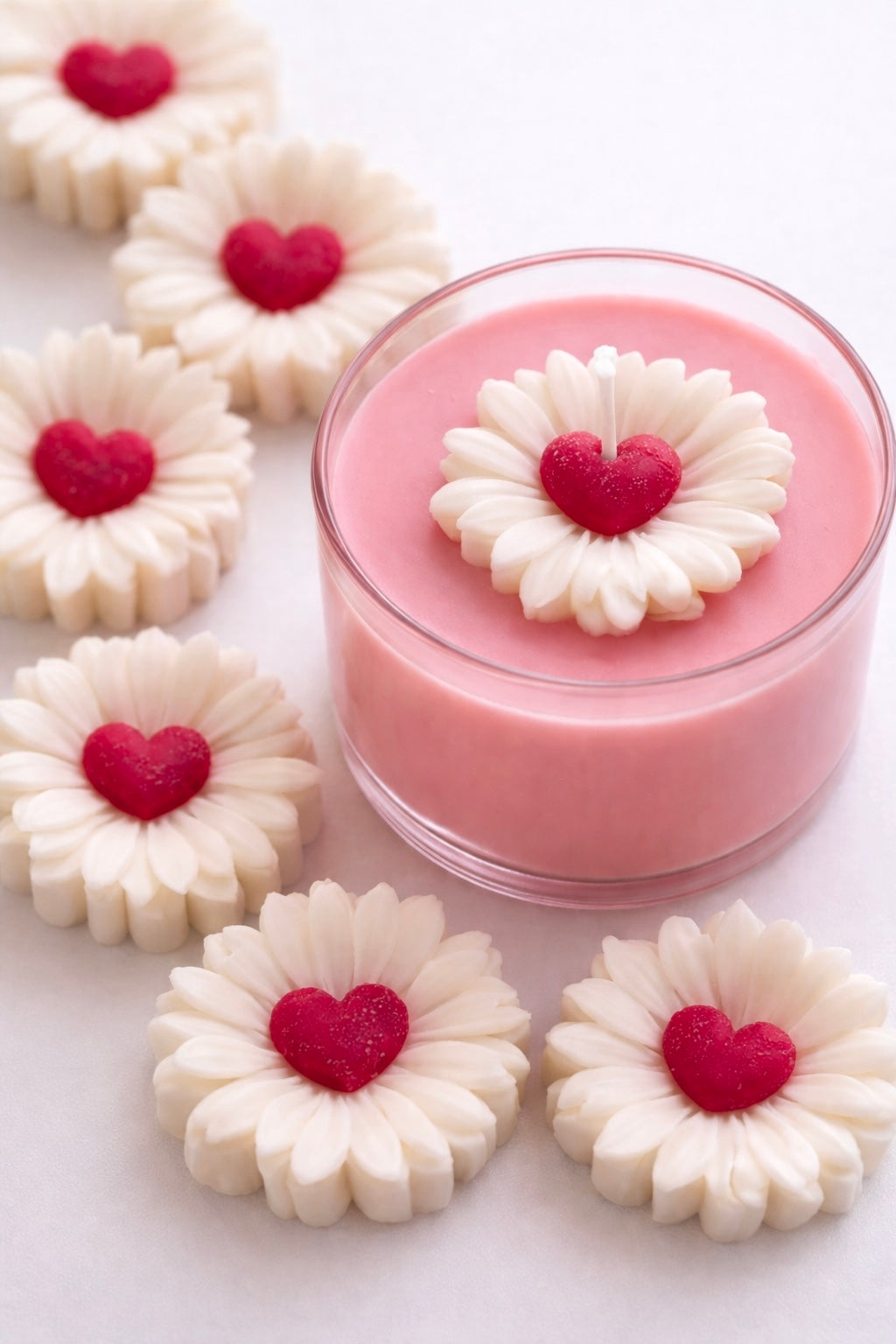 Pink candle with white sweetheart flower-shaped wax mold with red heart centers on a white background 