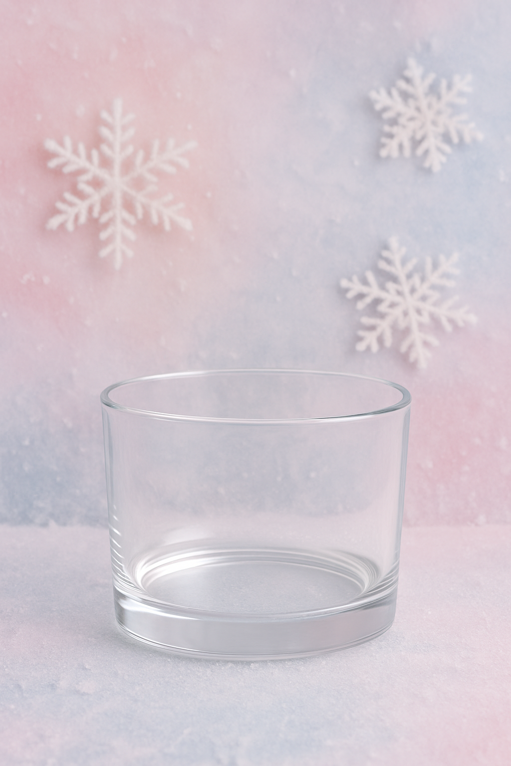 Clear glass candle vessel on a pastel gradient background with snowflake decorations