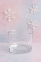 Clear glass candle vessel on a pastel gradient background with snowflake decorations