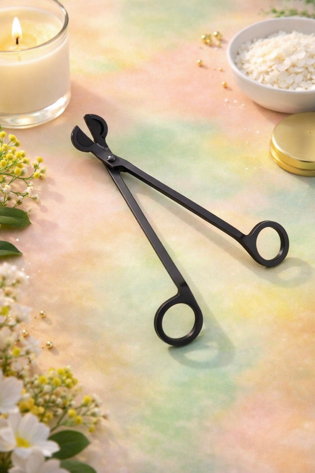Black wick trimmers on a colourful surface with flowers and a candle in the background