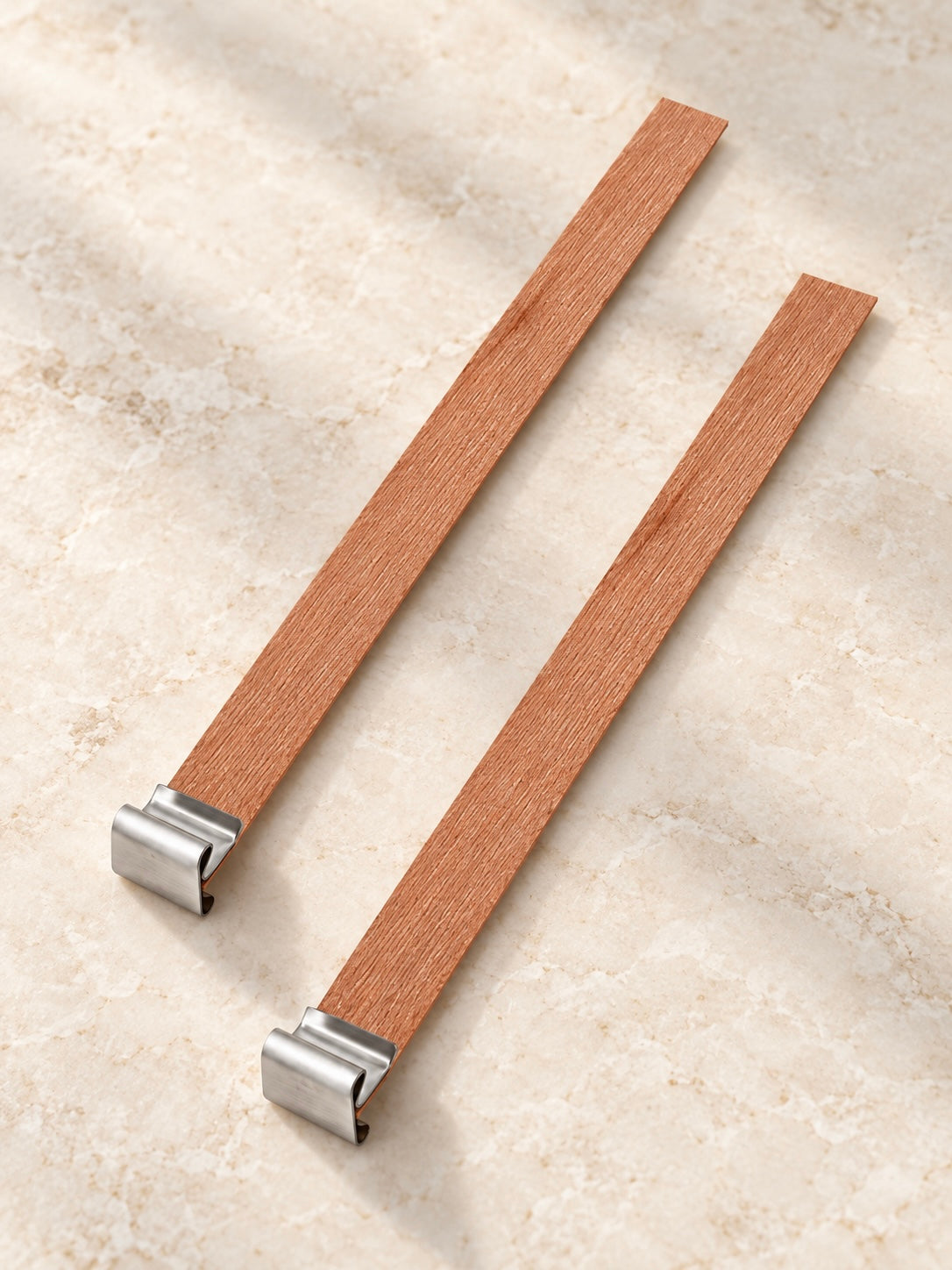 Two wooden wicks with metal wick clips on a light coloured marble surface 