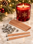 Wooden wicks with wick clips on a marble surface with a red snowflake candle and Christmas decor in the background. 