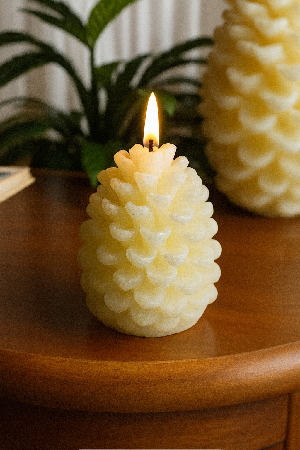 Pinecone candle with a lit wick on a wooden surface, with another similar candle in the background pinecone silicone mold used in candle making in Canada