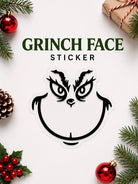 Grinch face sticker surrounded by Christmas decorations on a white background