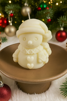 Snowman shaped candle on a stand with Christmas decorations in the background made from a Snowman Silicone Mold for candle making in Canada.